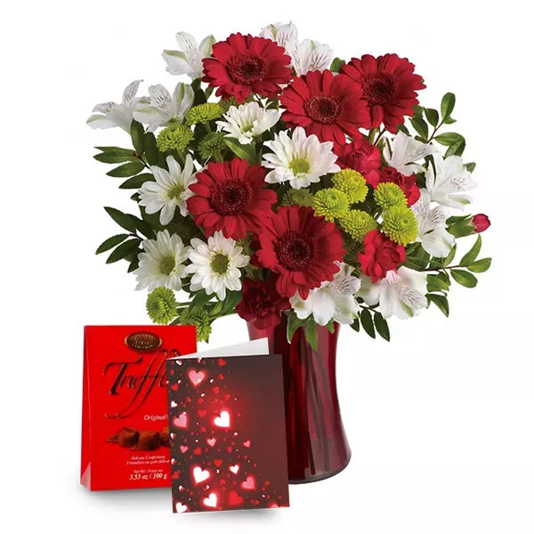 A bouquet of red and white flowers in a vase with a box of chocolates and a card with hearts.