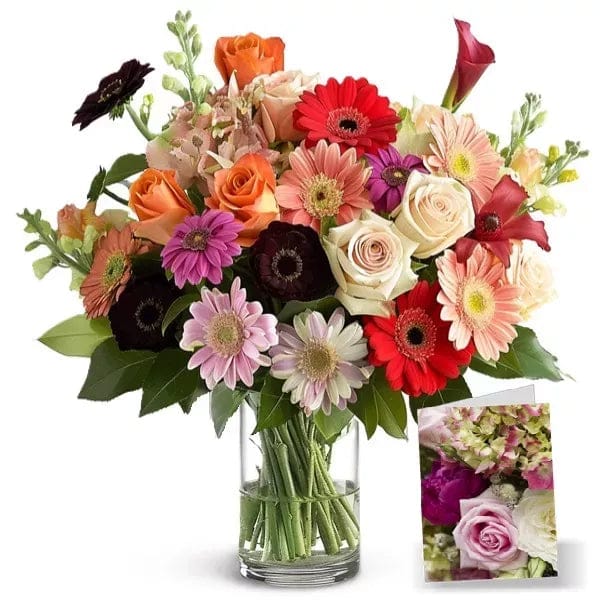 Bouquet of colorful roses and gerberas in glass vase with card.