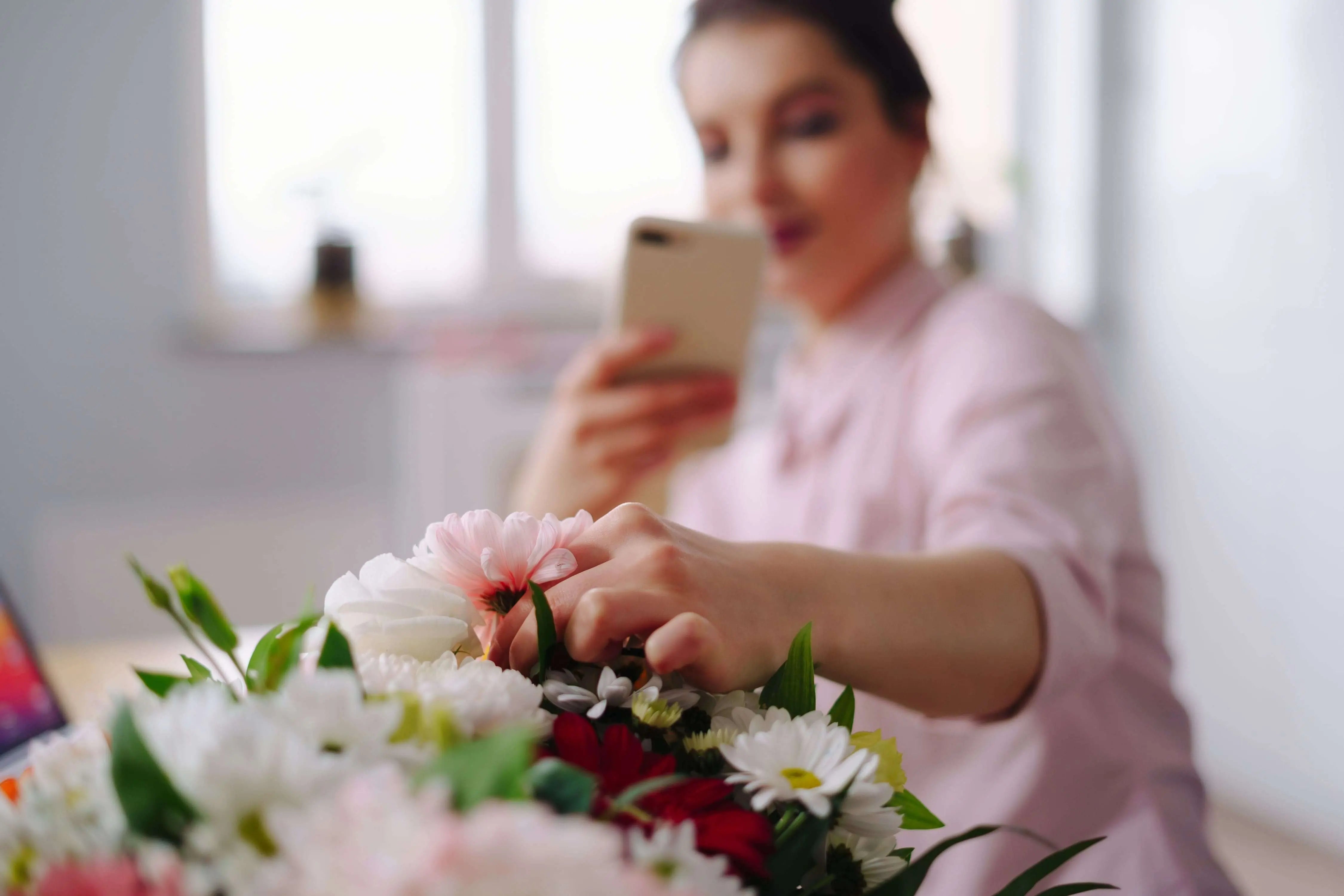 Woman arranging fresh flower bouquet, taking a photo.