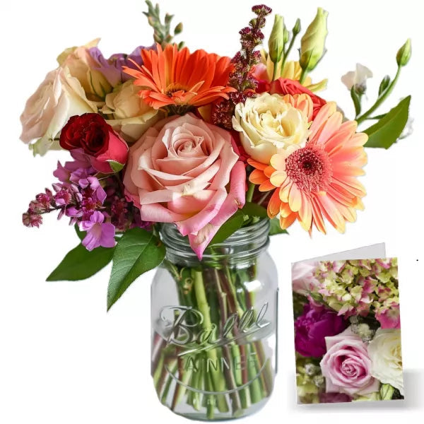 A colorful bouquet of mixed flowers in a mason jar, next to a small floral card.